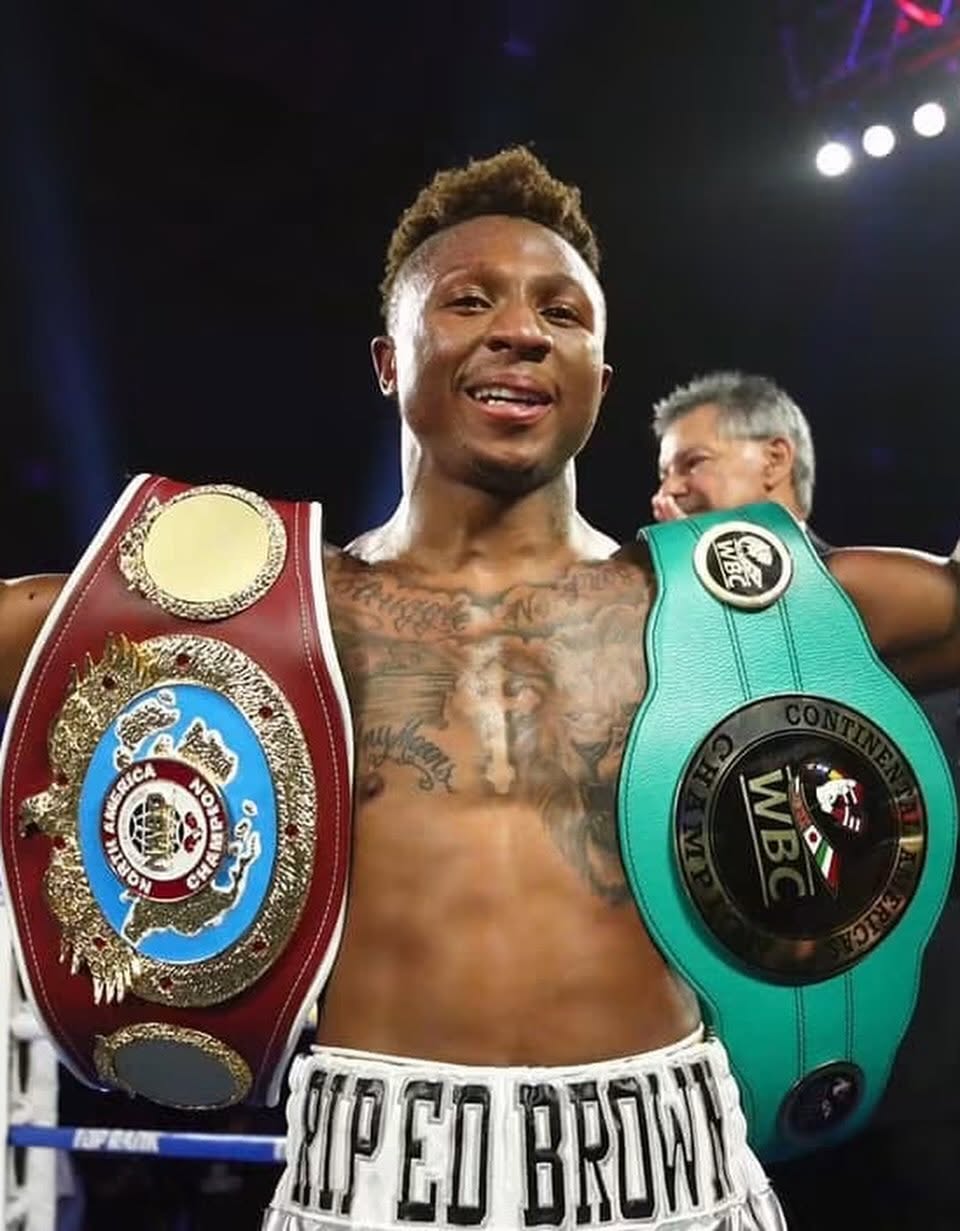 Professional boxer Joshua Greer Jr., bare-chested and smiling, draped with his NABO North America and WBC Continental Americas championship belts.