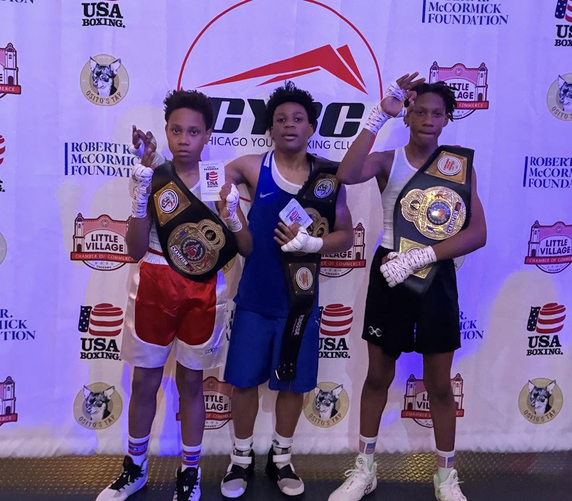 Three young boxers holding championship belts in front of a Chicago Youth Boxing Club backdrop.