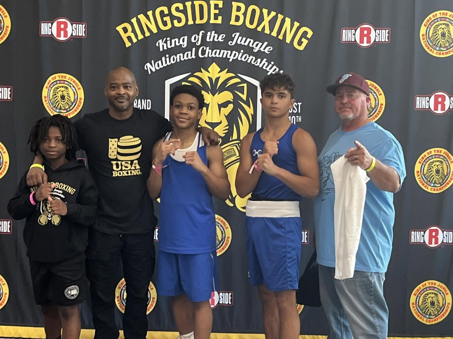 Coaches and three young boxers in front of a 'Ringside Boxing — King of the Jungle National Championship' backdrop.
