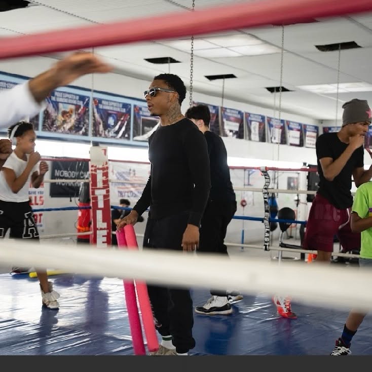 A coach inside the ring supervising a youth training session as several kids shadowbox around him.