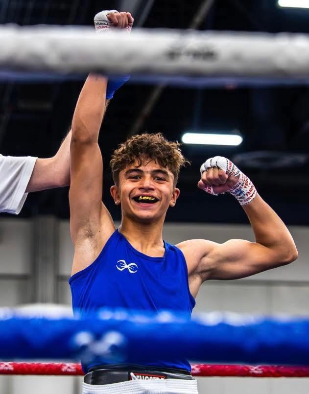 A teenage boy boxer celebrating a win in the ring as the referee raises his arm.